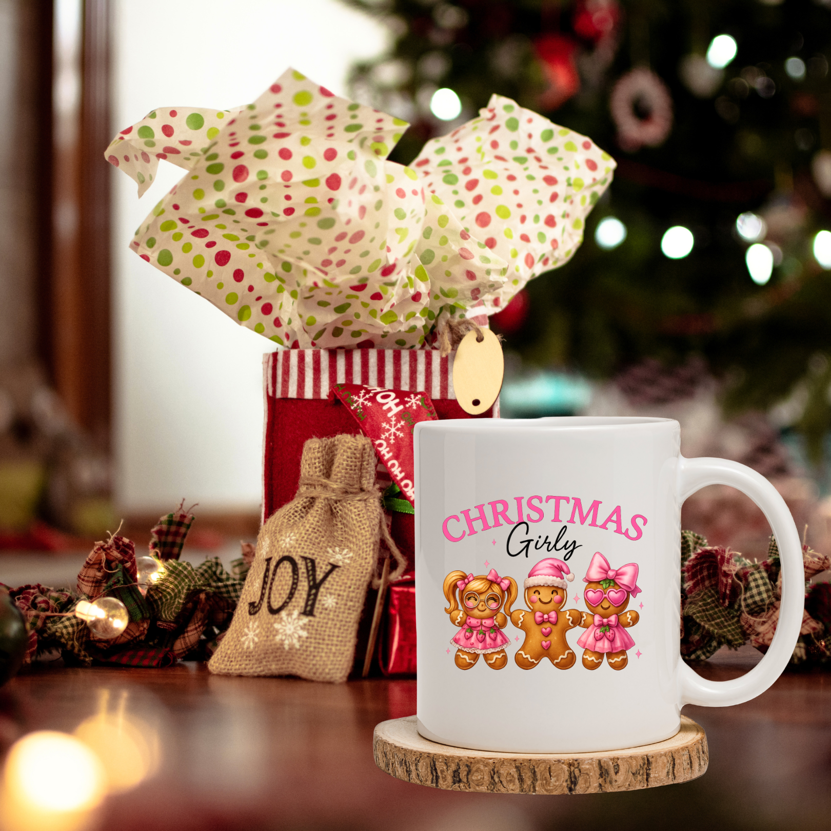 White mug with three gingerbreads and words "Christmas Girly' design, wrapped gift, and Christmas tree in the background