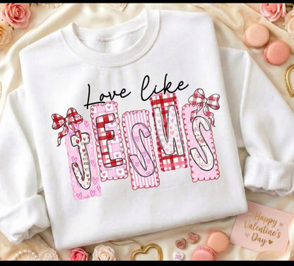 White Valentine sweatshirt featuring a Love Like Jesus design with patchwork lettering, bows, and soft heart details in a faith-inspired style.